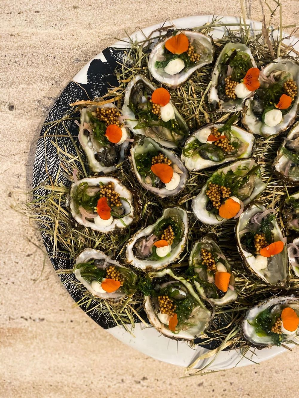 Schaal verse oesters op hooi, afgewerkt met zeewier, mosterdzaad en bloemblaadjes