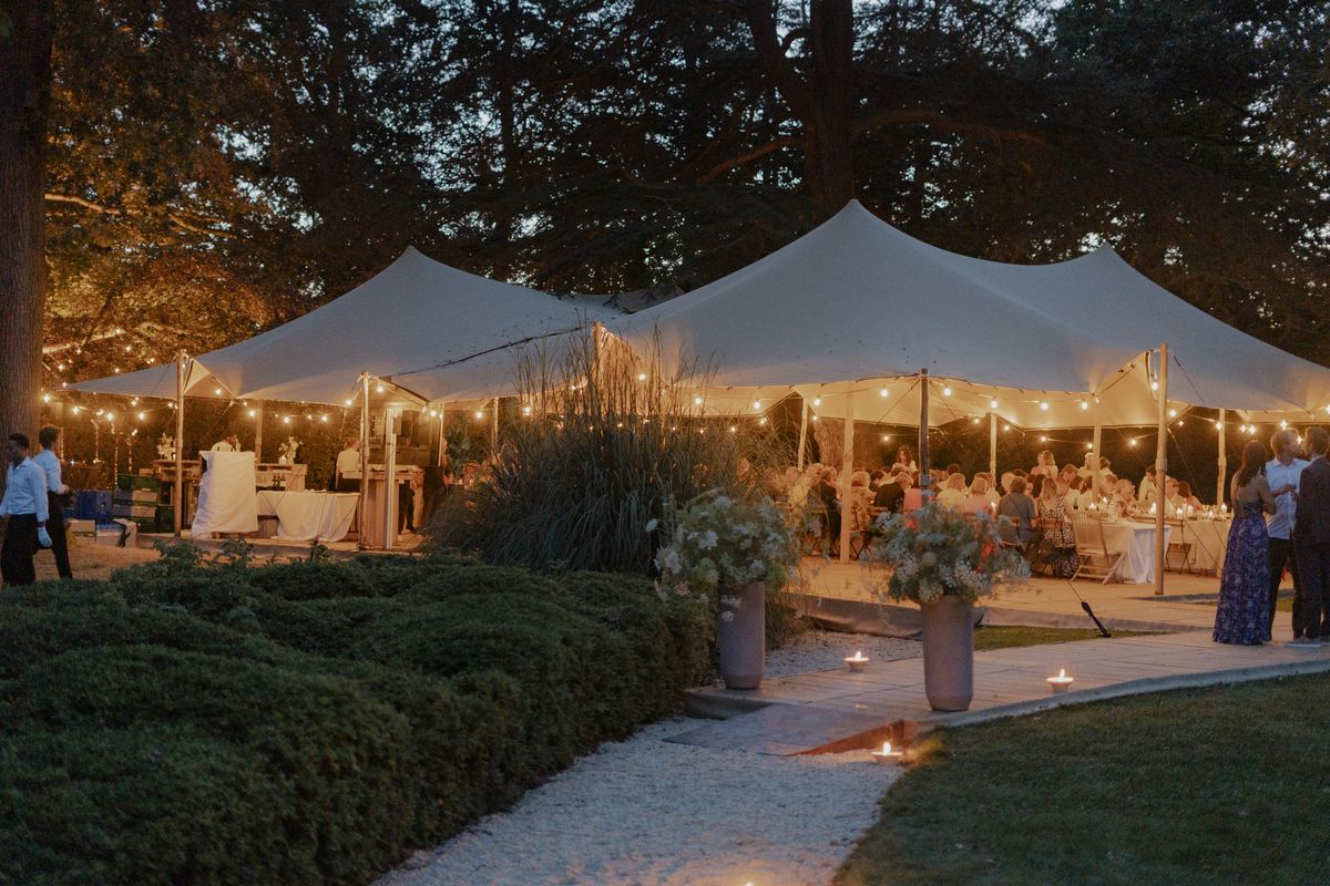 Verlichte feesttenten met lange tafels in een tuin bij valavond