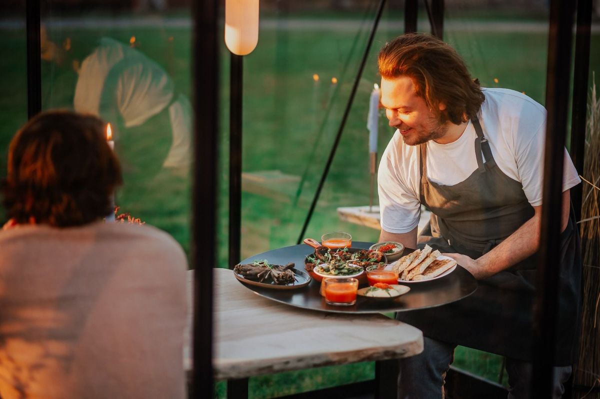 Chef serveert een deelplank aan tafel in een glazen tuinkamer
